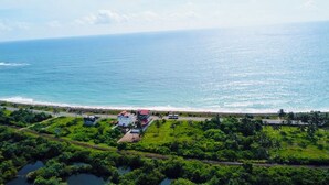 An aerial view of a coastal area with a beach, a road, and a cluster of buildings with a red roof. - Ocean Front Villa (Hikkaduwa)