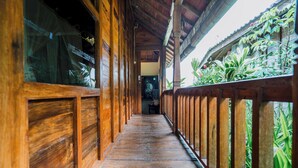 Un couloir en bois, avec une rambarde en bois d’un côté, et une vue sur la verdure à l’extérieur.