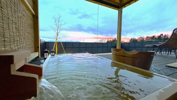 Uma banheira de hidromassagem com vista para o pôr do sol, um espaço de estar coberto e um deck de madeira.