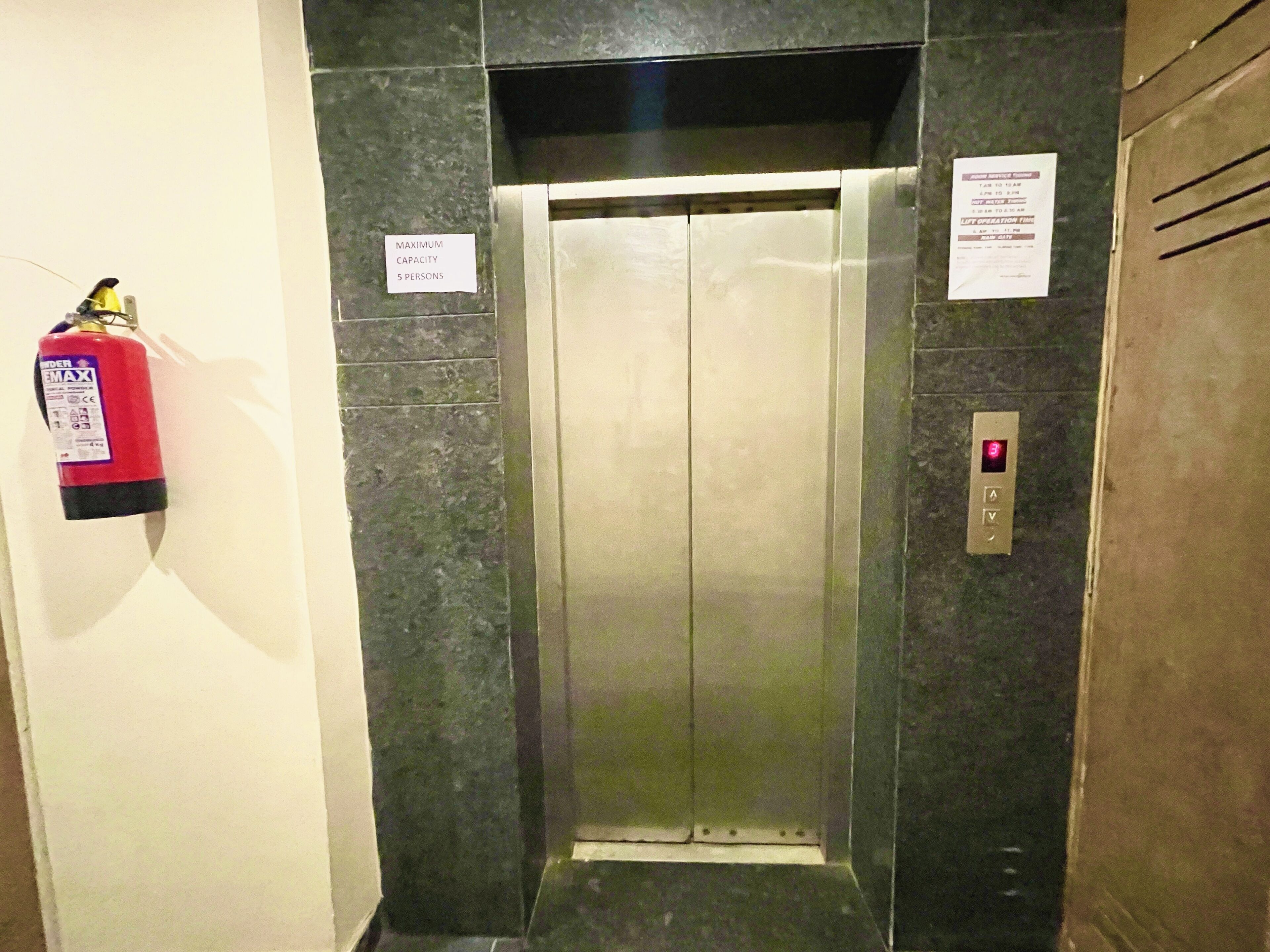 Un ascensor con un cartel de capacidad máxima, un extintor y un panel de control.