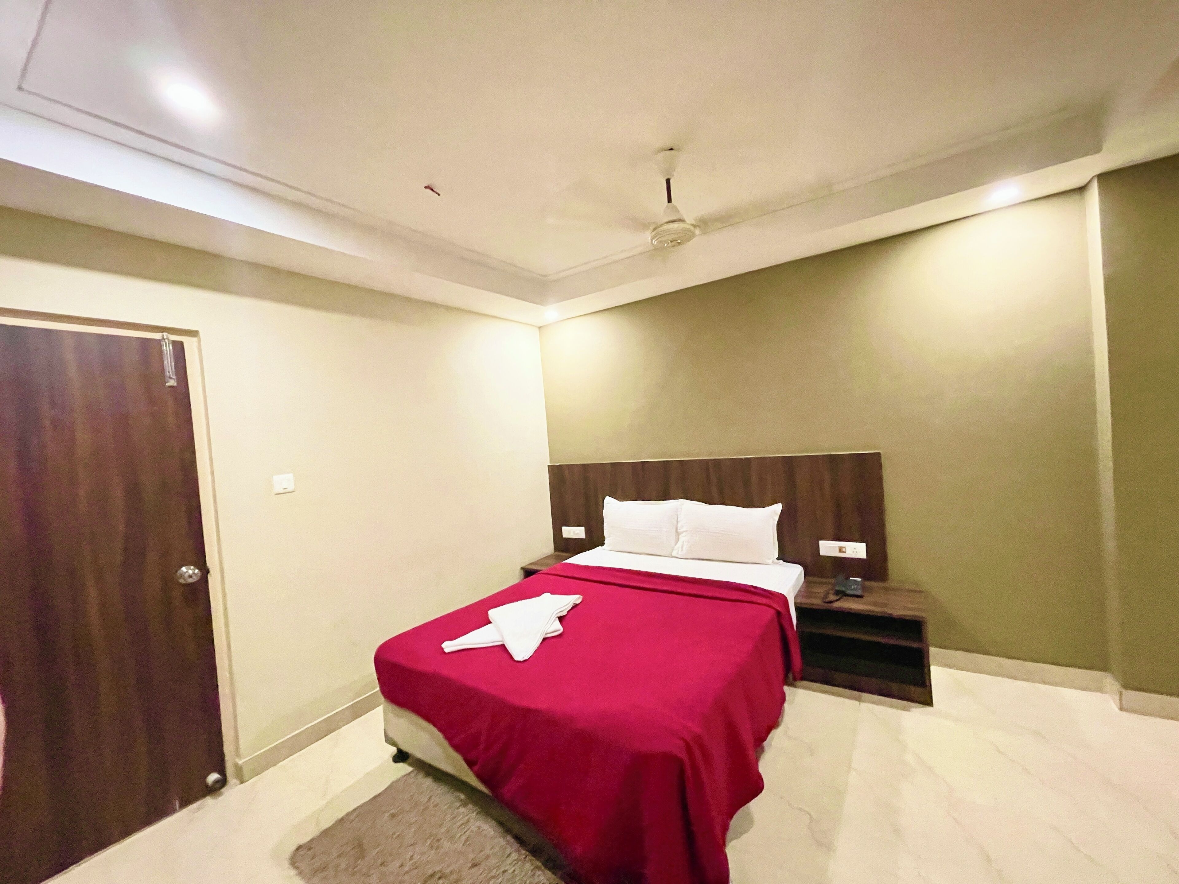 Una habitación de hotel con cama, mesita de noche, puerta de madera y ventilador de techo.