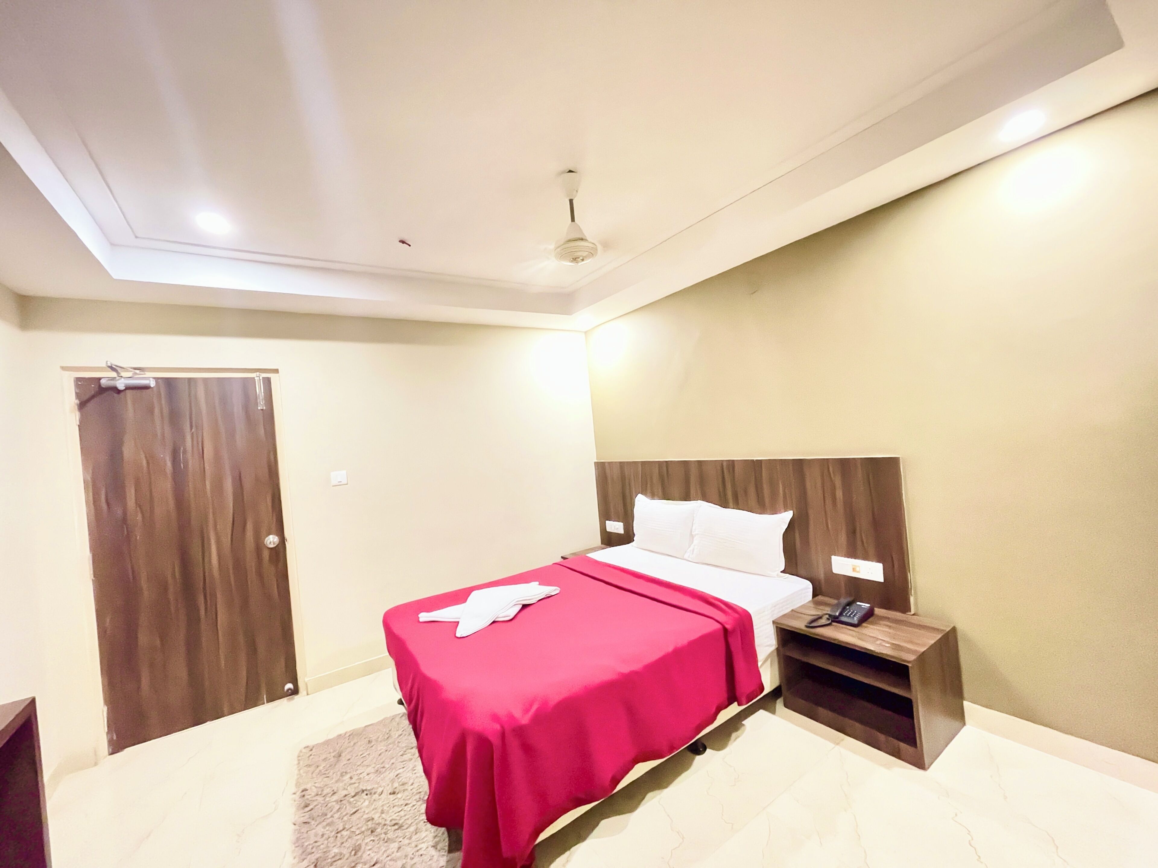 A hotel room with a bed, a bedside table with a phone, and a door.