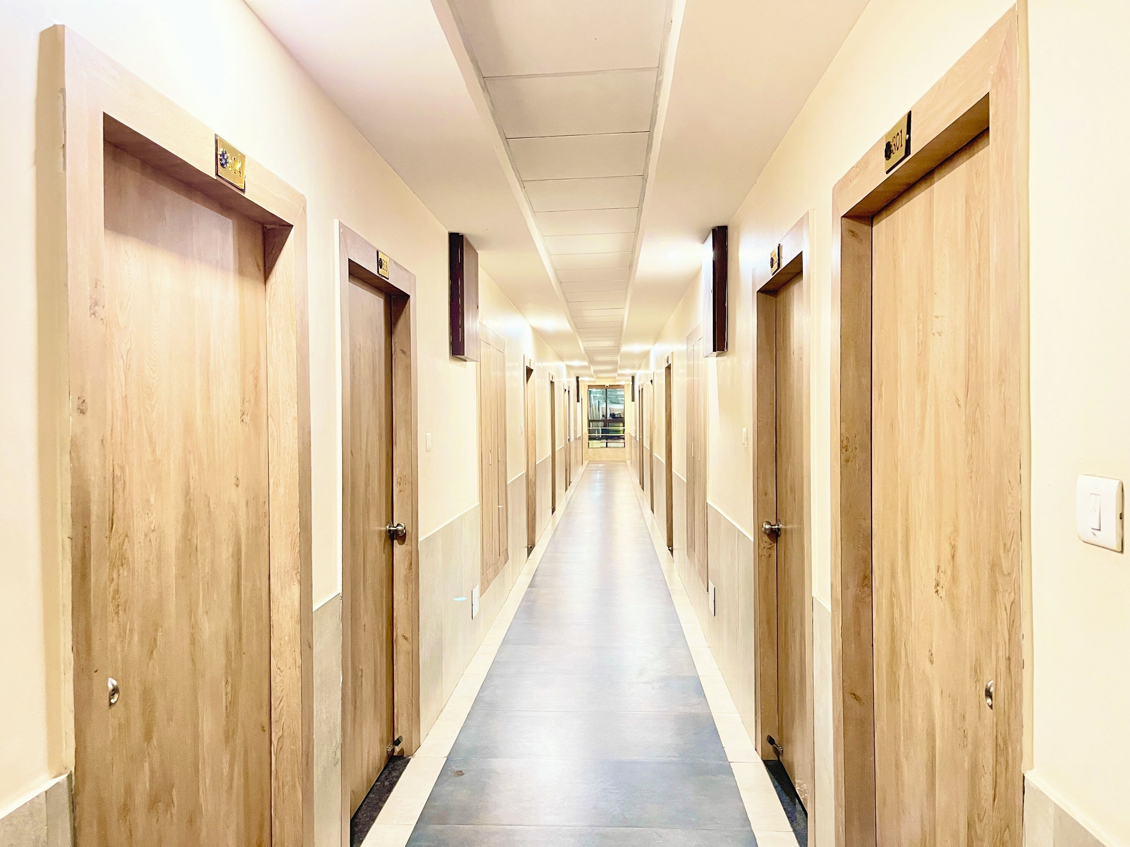 Un long couloir étroit, typique d’un hôtel, avec des portes en bois de chaque côté et un sol carrelé.
