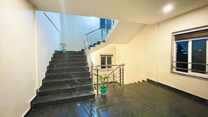 A staircase leading to an upper floor with a handrail, a potted plant, and a window with a view of the outside. - Hotel Janaki Pride - near Temple (Puri)