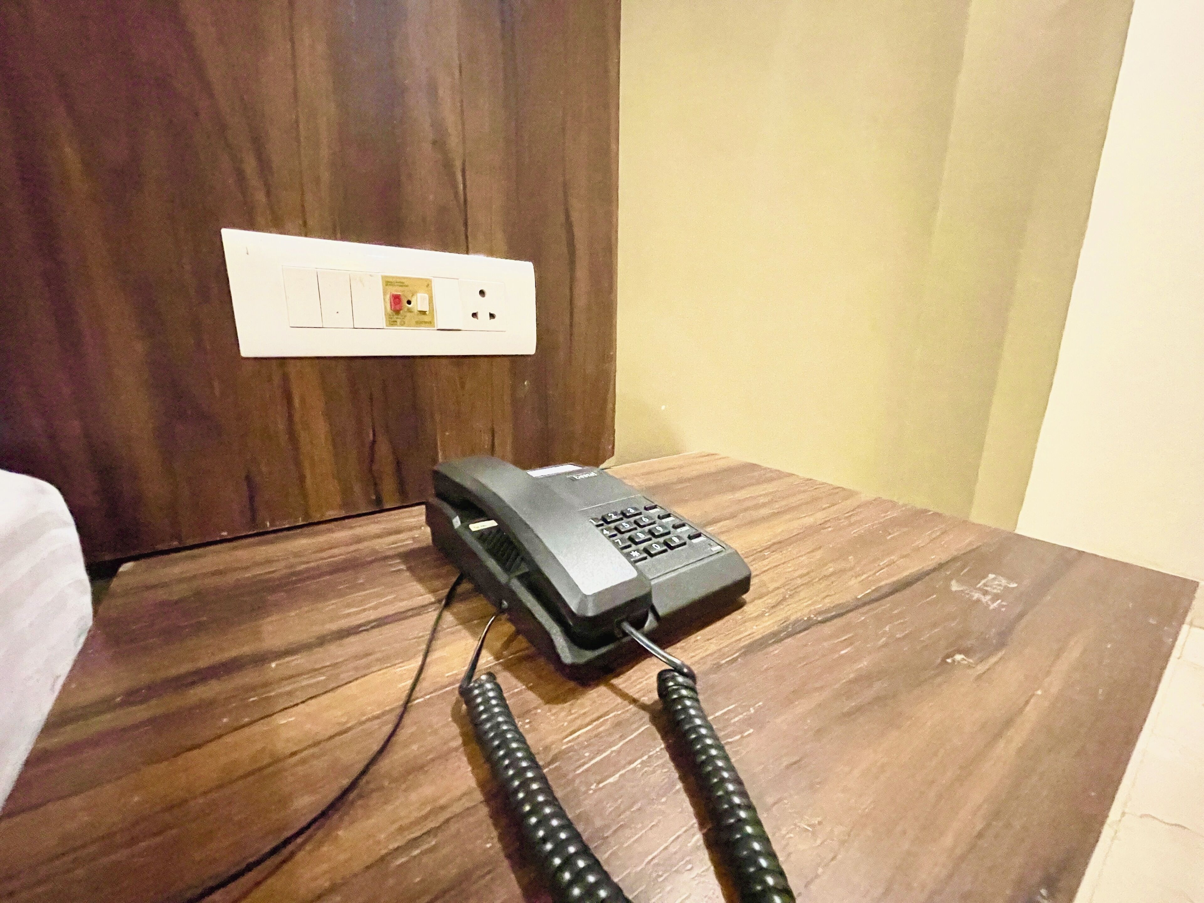 Een telefoon op een houten nachtkastje, met een stopcontact op de achtergrond.