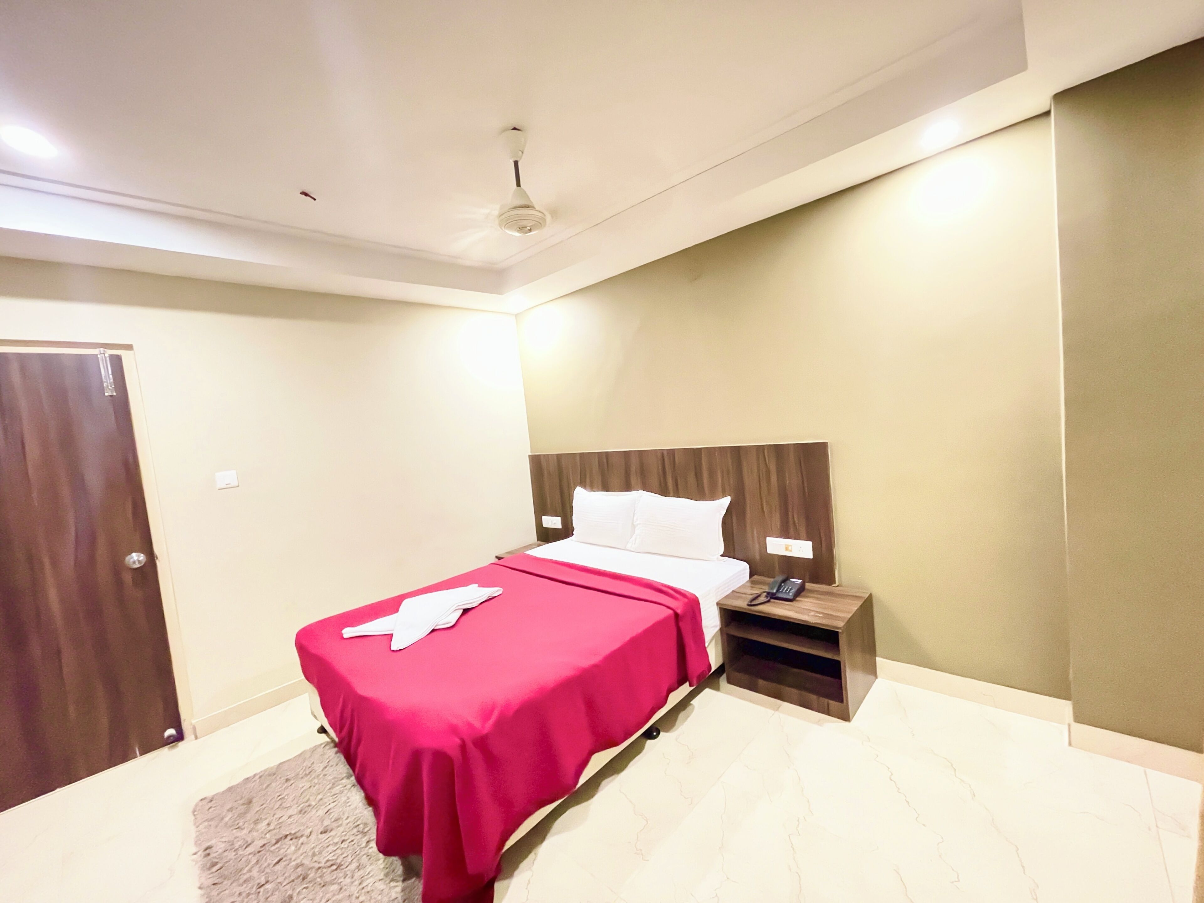 A hotel room with a bed, a nightstand, a telephone, and a door.