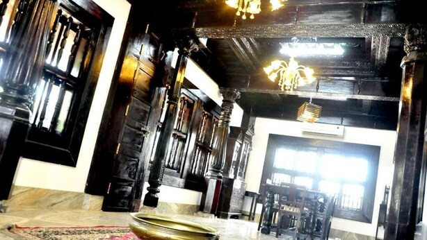 A traditional interior with ornate wooden pillars, a large ornate mirror, and a patterned rug on the floor. - Heritage Villa (Mangaluru)