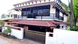 A two-story house with a red-tiled roof, a balcony with black railings, and a white exterior wall. - Heritage Villa (Mangaluru)