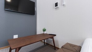 Ett rum med en platt-TV som är monterad på väggen, ett litet bord med en krukväxt och en fjärrkontroll på bordet.