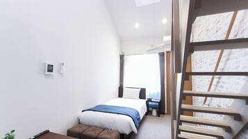 A modern hotel room with a bed, a desk, a chair, a small table, and a staircase.