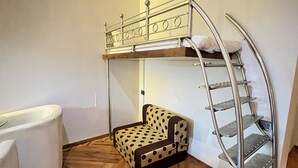 Een stapelbed met een ladder, een streephanddoek sofa en een witte stoel in een kamer met houten vloeren en een airconditioning aan de muur.