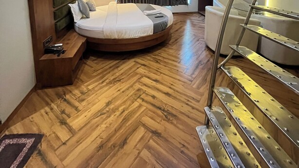 Een moderne hotelkamer met een rond bed, houten vloeren, een ingebouwde bank, een bureau, een spiegel, een plafondventilator, een trap en een raam met gordijnen.