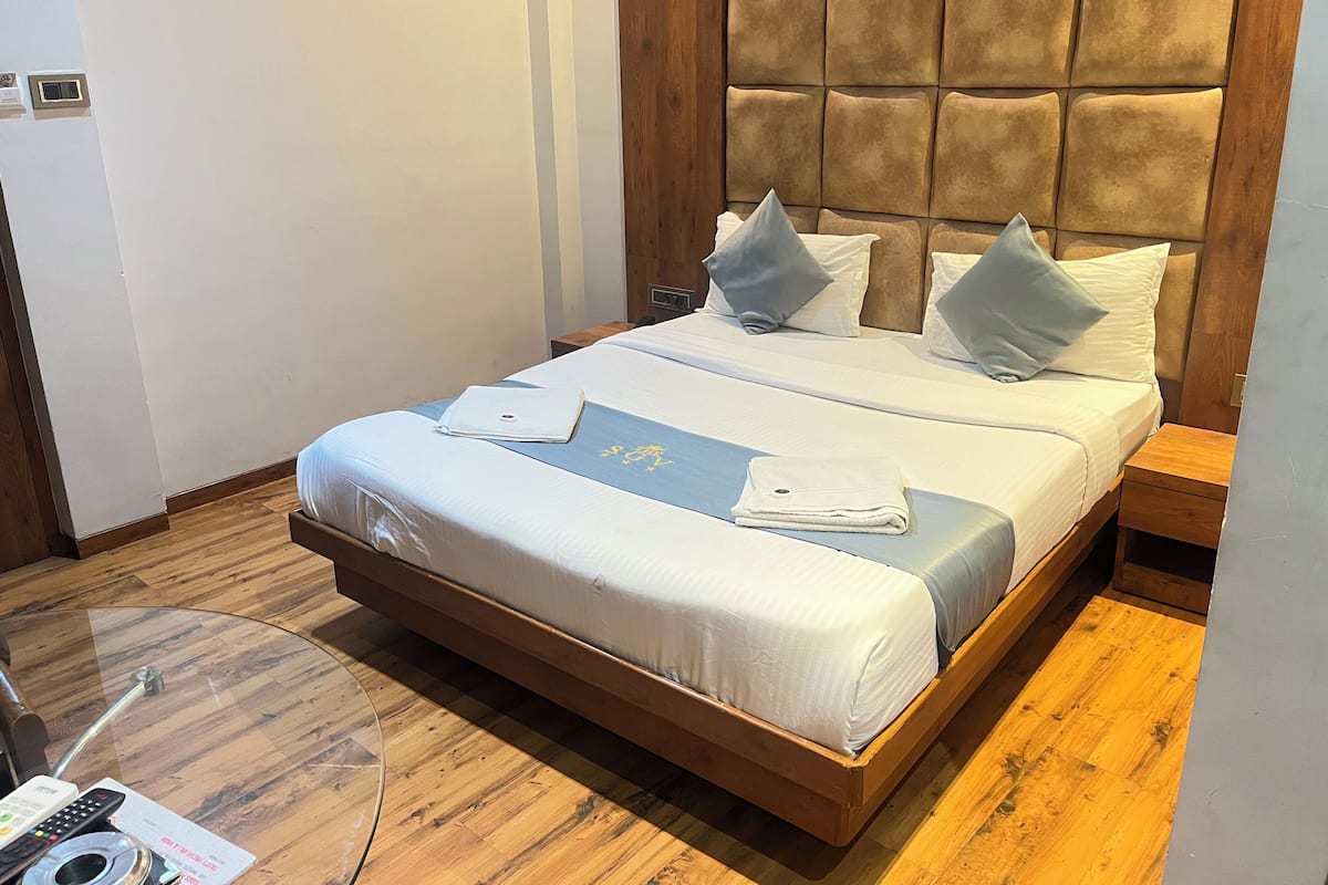 A neatly made bed with a headboard, a bedside table, and a small table with a remote control and a menu card.