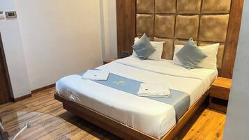 Una cama bien hecha con cabecera, una mesita de noche y una pequeña mesa con un control remoto y una tarjeta de menú.