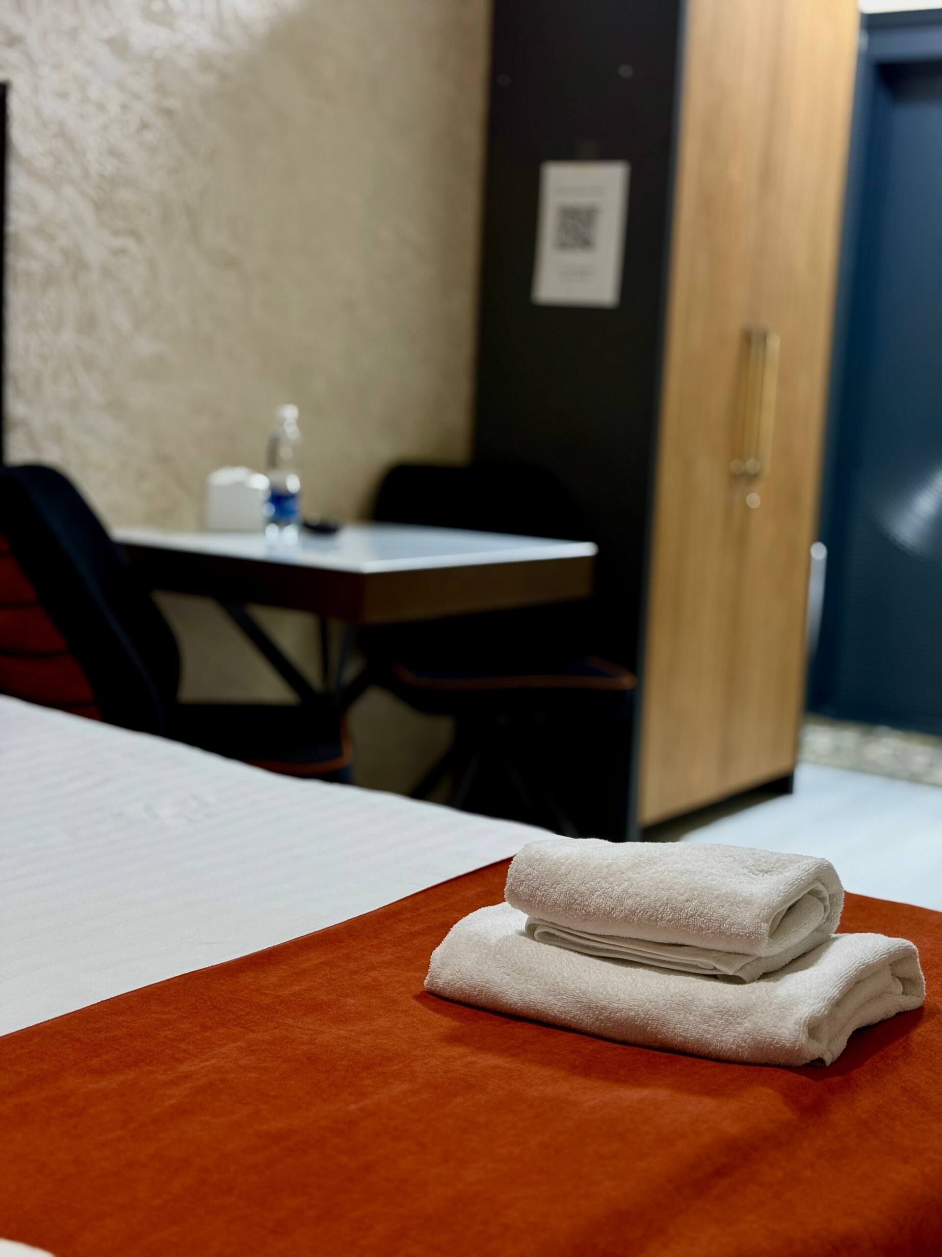 A hotel room with a bed, a table with a bottle, and a door.