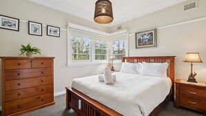 Une chambre à coucher avec un grand lit, une commode en bois, une table de chevet avec une lampe et des tableaux encadrés accrochés au mur.
