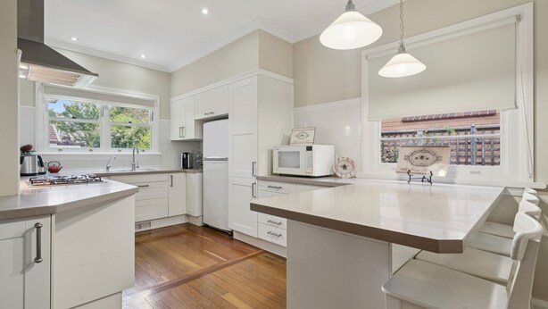 Une cuisine moderne avec des meubles blancs, un îlot central et des luminaires suspendus.