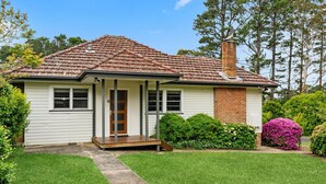 Une maison de plain-pied avec un toit en tuiles, une cheminée en briques et un porche à l’avant.