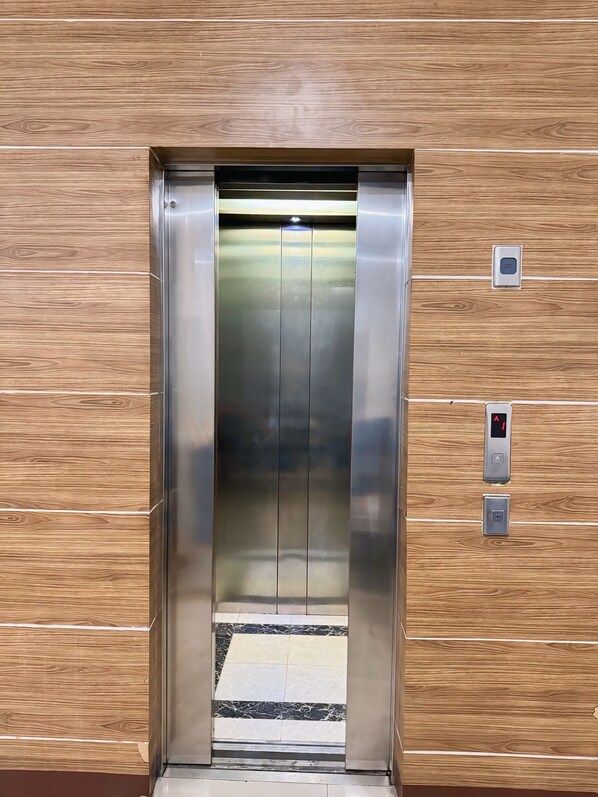An elevator with a metallic interior and a wooden panel wall. - Stay 'd Pondok Indah (Jakarta)