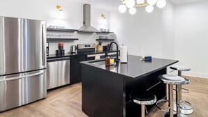 Une cuisine moderne dotée d’appareils électroménagers en acier inoxydable, d’un îlot central noir, de tabourets de bar et d’un lustre.