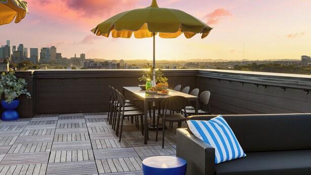A rooftop terrace with a dining table, chairs, a sofa, and an umbrella.