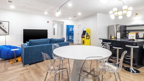 A modern interior with a round dining table, clear chairs, a blue sofa, and a kitchen area with a refrigerator and bar stools. - The Carter Buyout - 2 Units by AvantStay | Group Stays (Nashville)