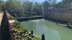 A serene water feature with a stone wall and greenery, a clear sky, and a distant building. - Appartement hotel (Castera-Verduzan)