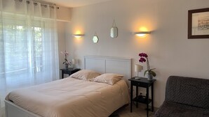 A bedroom with a bed, bedside tables, lamps, and a chair. - Appartement hotel (Castera-Verduzan)