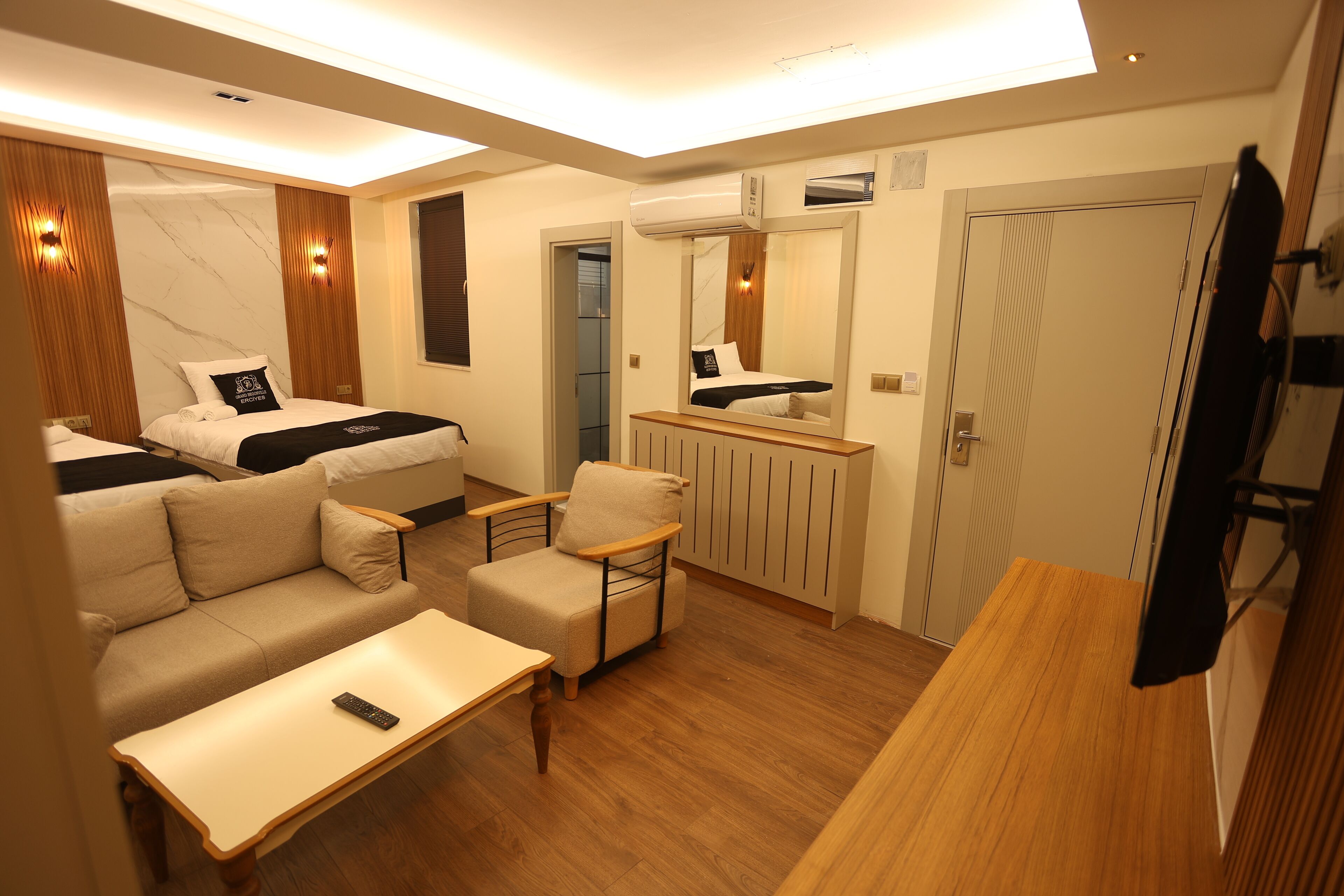 Ein kleines Hotelzimmer mit Schlafgelegenheit, Sofa, Tisch, Stuhl, Spiegel und Fernseher.