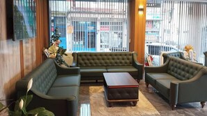 A lobby with a green sofa set, a wooden accent wall, a flat-screen TV, and a large window with a view of the street. - Grand Begonville Erciyes Hotel (Develi)