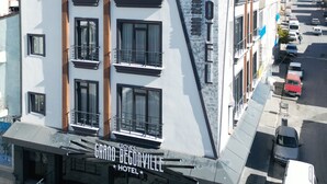 A modern hotel with a prominent sign reading "Grand Begonaville Hotel". It features multiple floors with balconies, a flat roof, and a parking area visible in front. - Grand Begonville Erciyes Hotel (Develi)