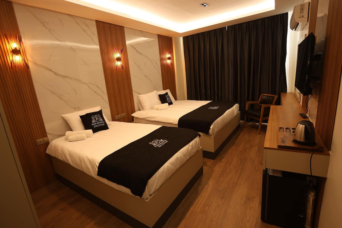 Quarto de hotel com duas camas, uma secretária com chaleira e televisão.