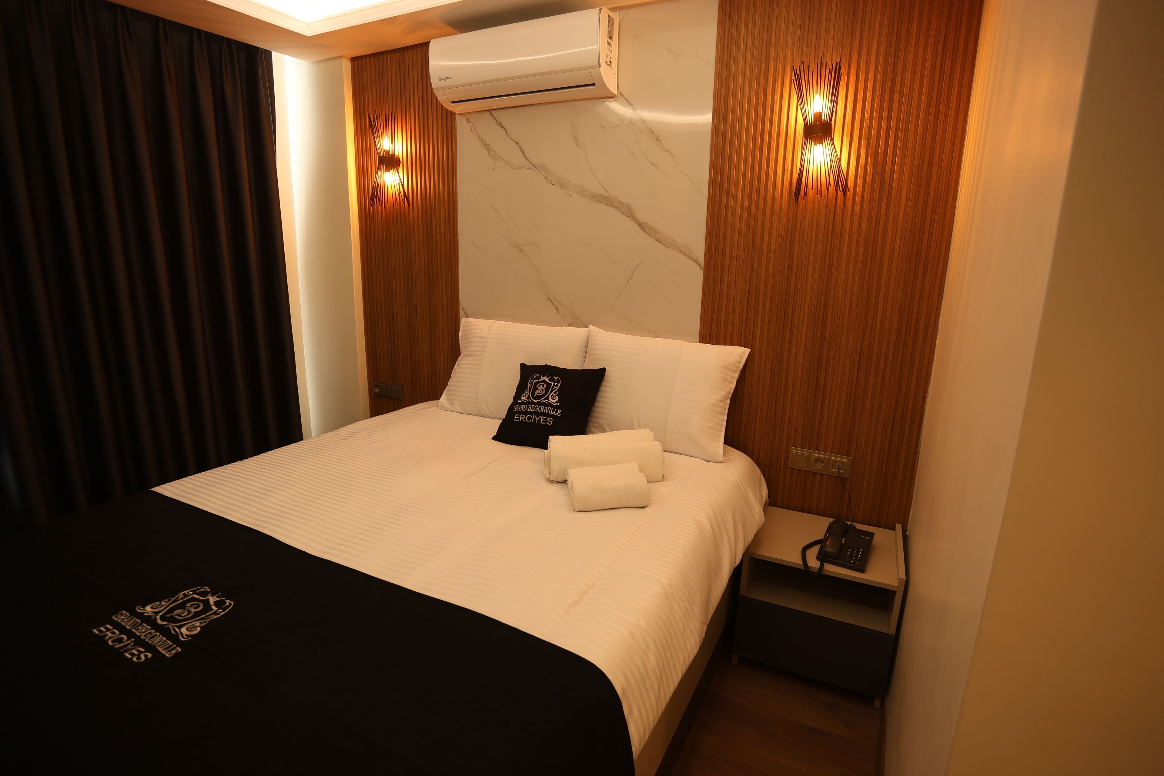 Une chambre d’hôtel équipée d’un lit, d’une table de chevet, d’un climatiseur et d’un luminaire fixé au mur.