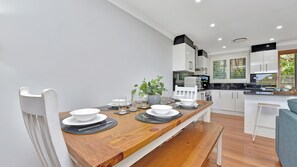 A modern kitchen with white cabinets, a wooden dining table with black placemats, and a potted plant.