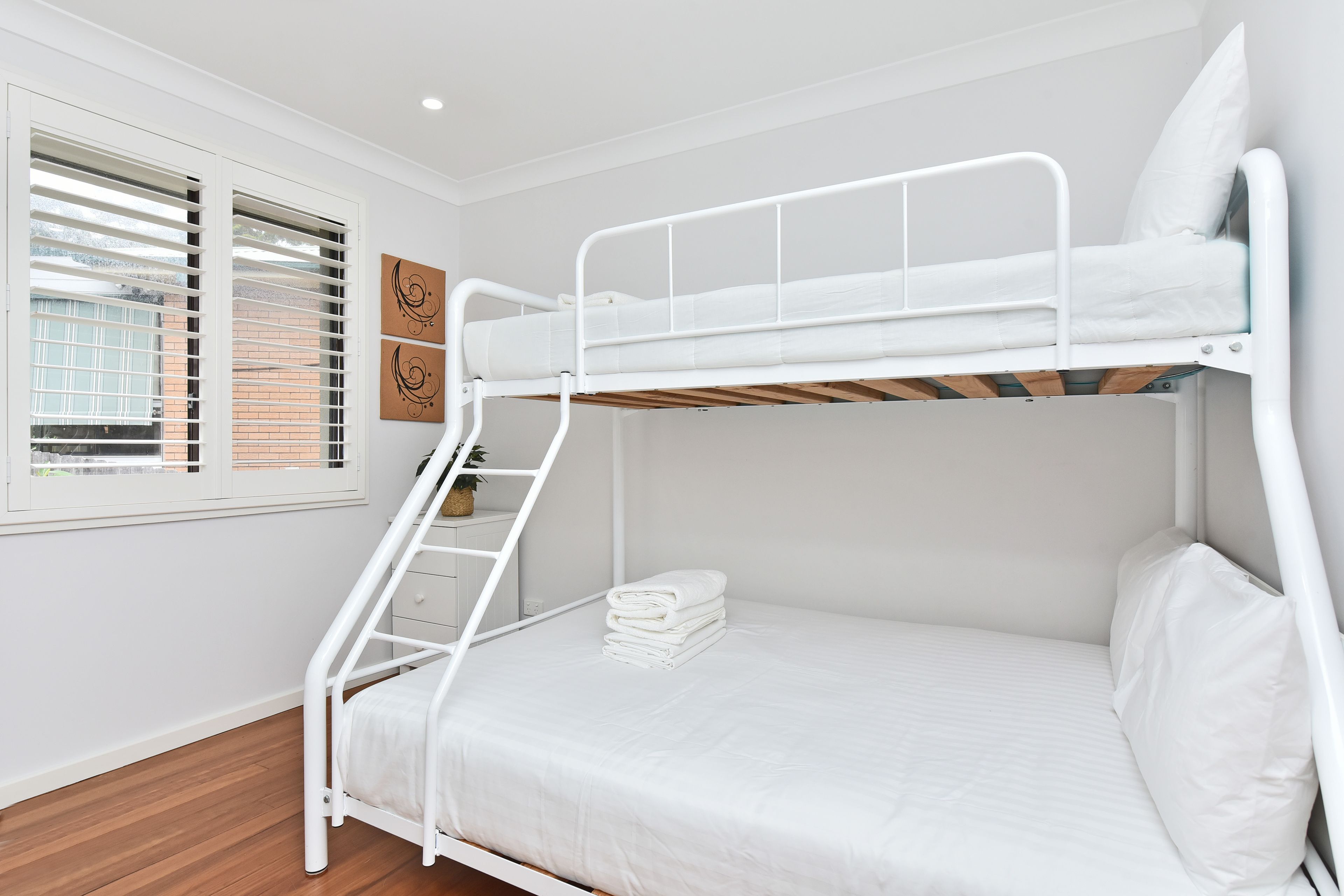Ein Stockbett mit einer Leiter, ein Fenster mit Jalousien und eine Wand mit zwei Dekorationselementen.