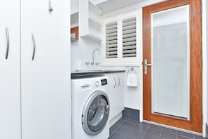 A modern laundry room with a Bosch washing machine, wooden door, and white cabinetry.
