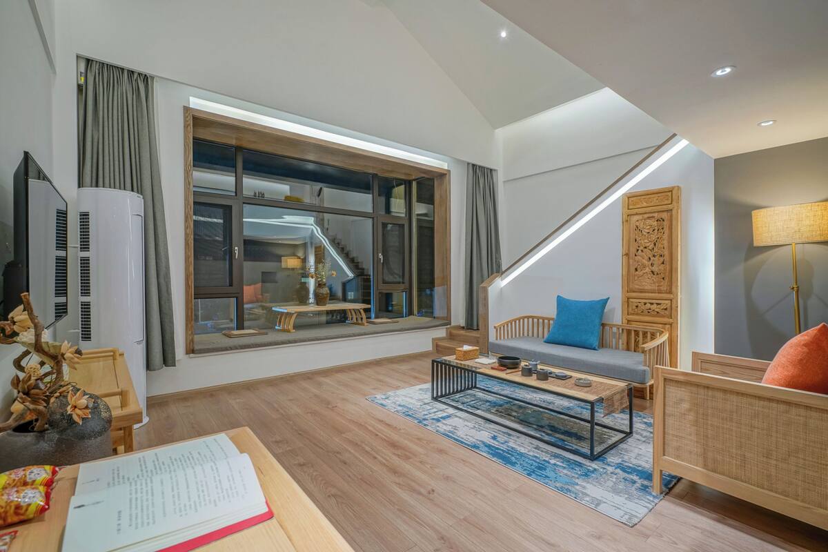 Una sala de estar moderna con un ventanal grande, una escalera y un sofá con cojines.