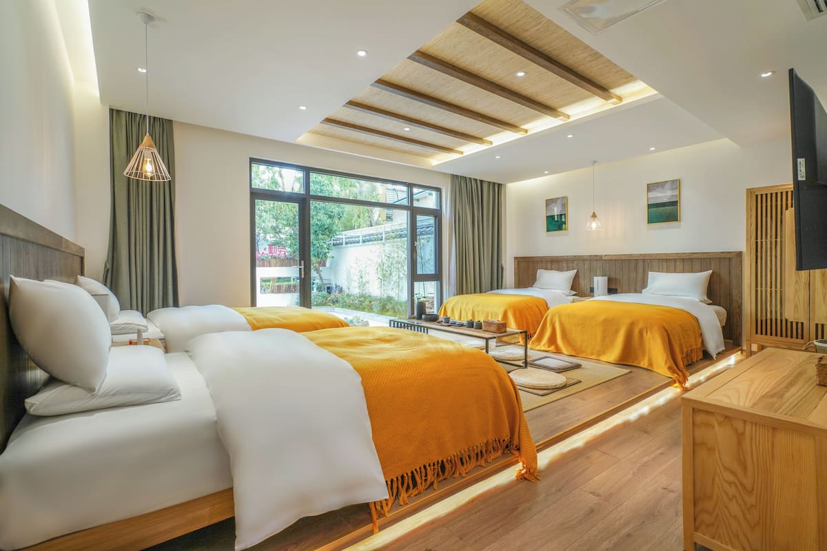 Habitación de hotel con dos camas, techo de madera, ventanas amplias y un televisor.