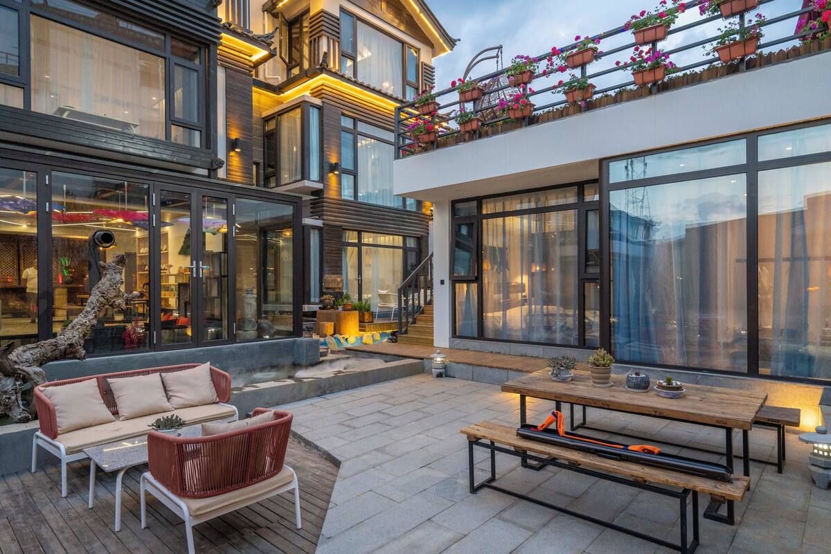 Un patio exterior moderno con una mesa y bancos de madera, un sofá y un árbol decorativo.