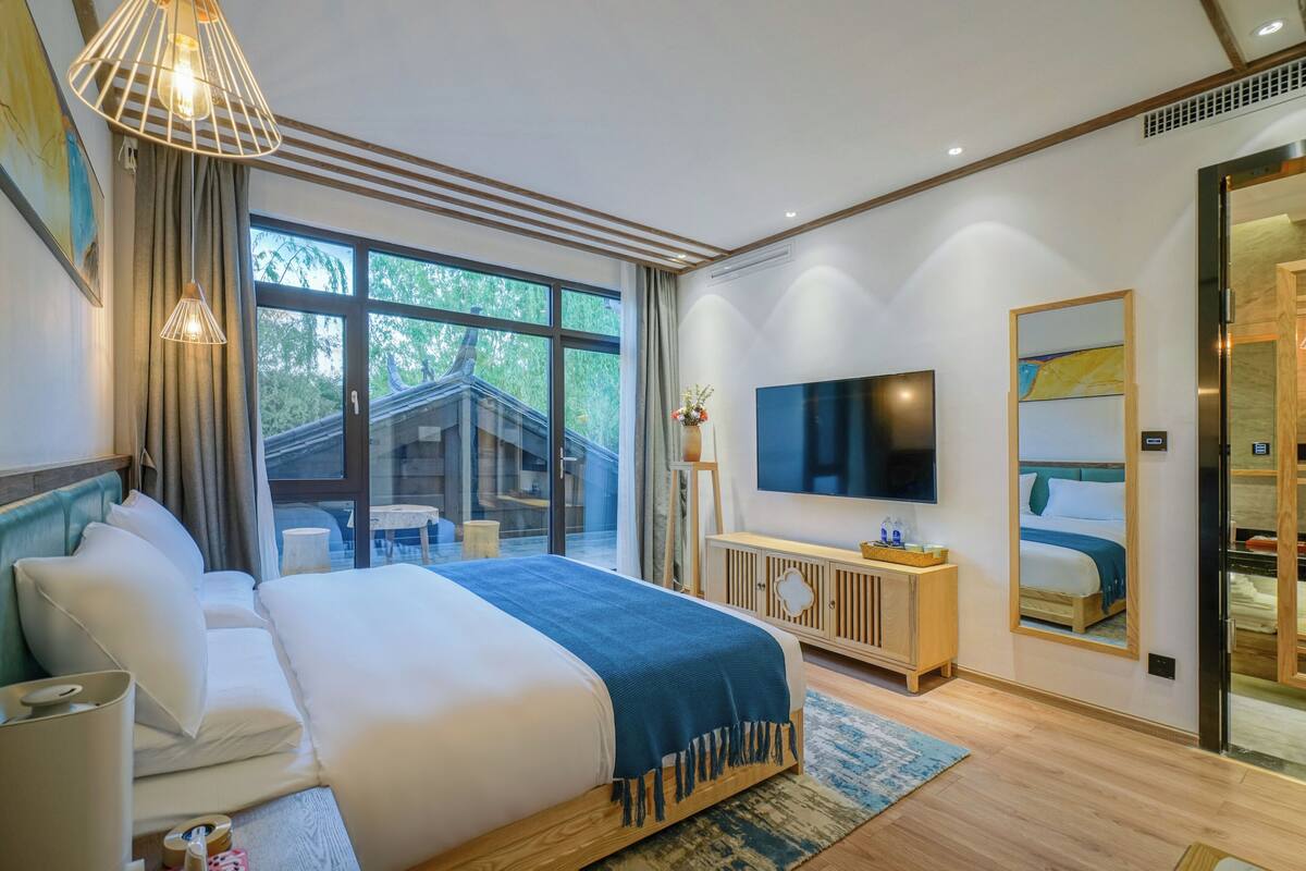 Habitación de hotel moderna con una cama grande, televisión, aparador de madera y un ventanal que ofrece vistas al exterior.
