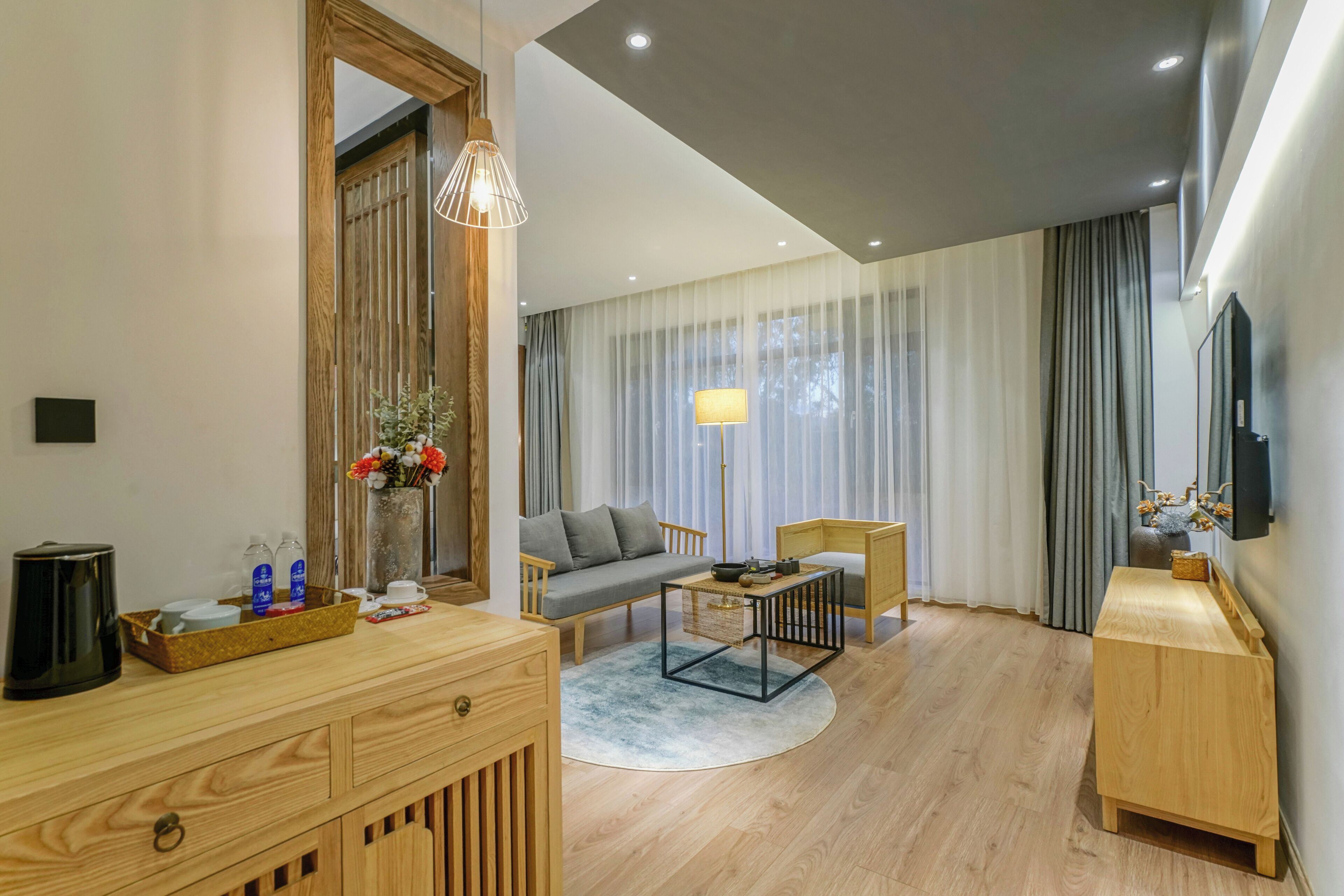 A modern hotel room with a wooden desk, a sofa, a coffee table, and a TV mounted on the wall.