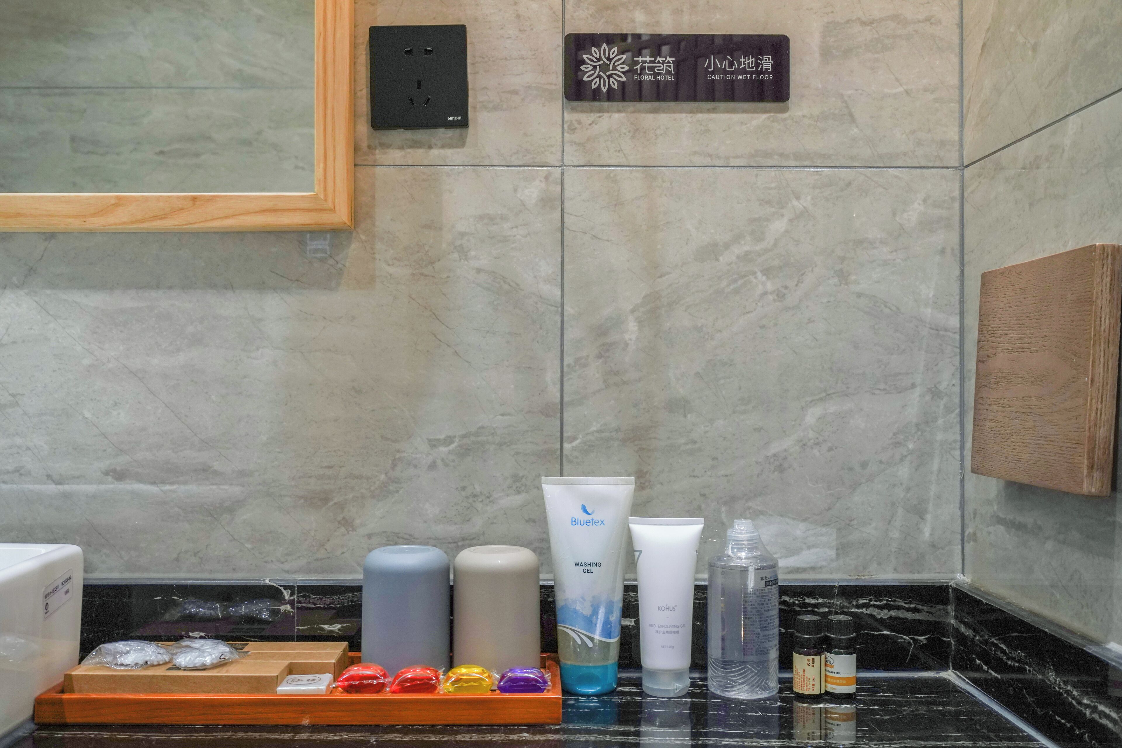 Une salle de bain avec un mur en marbre, un meuble en bois et une étagère contenant des articles de toilette, notamment un gel lavant Bluetex et un flacon de savon liquide.