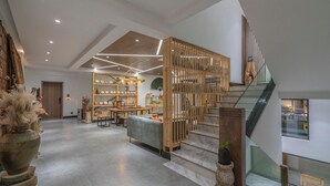 A spacious lobby with a wooden staircase, a seating area with tables, and a decorative wall. - Lijiang Xisu Garden (Lijiang)