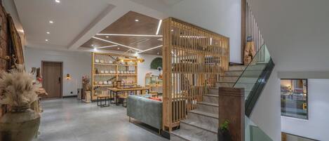 Un hall espacioso con una escalera de madera, una zona de estar con mesas y una pared decorativa.