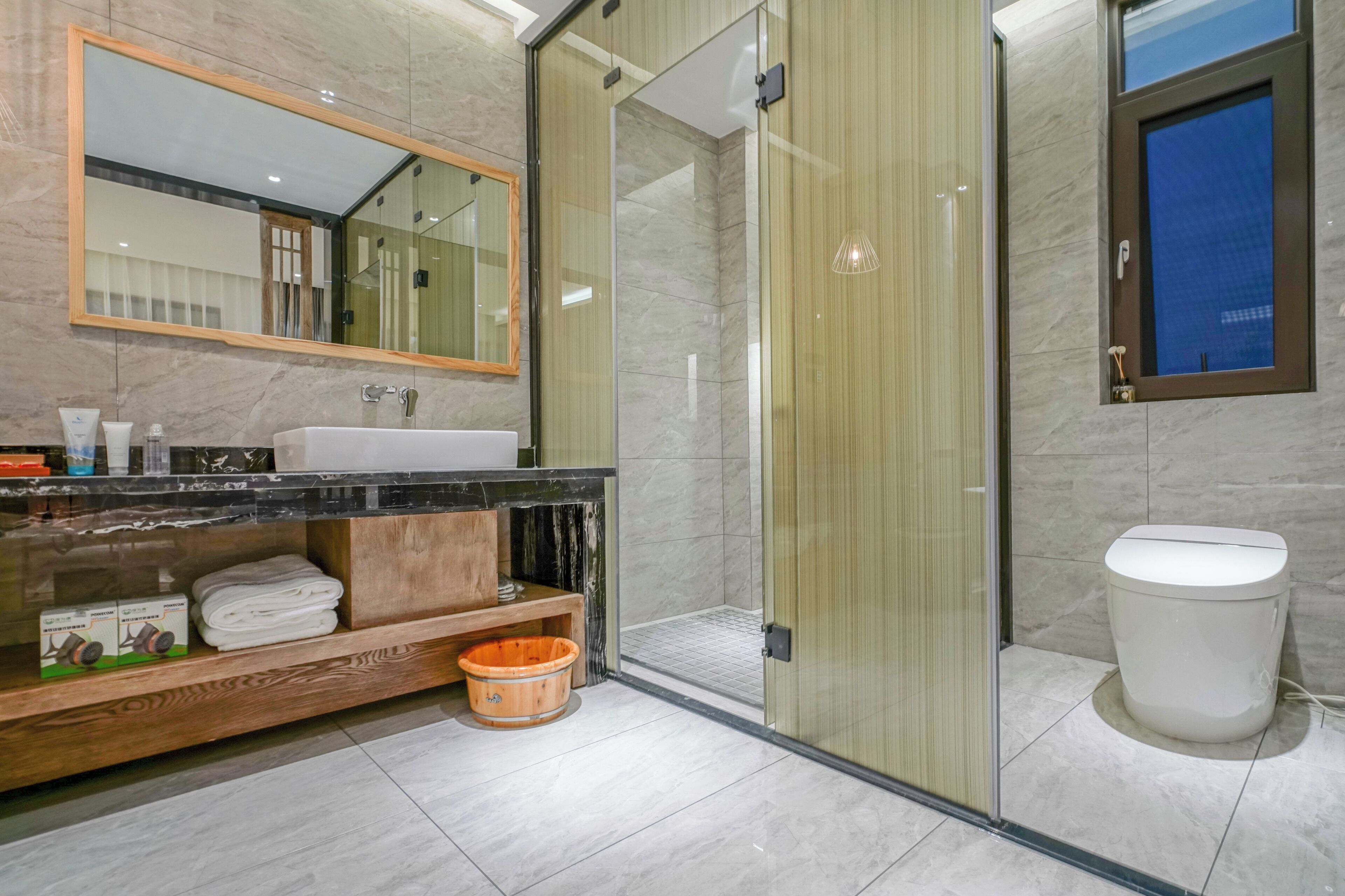 A modern bathroom with a marble sink, a glass shower enclosure, and a toilet.