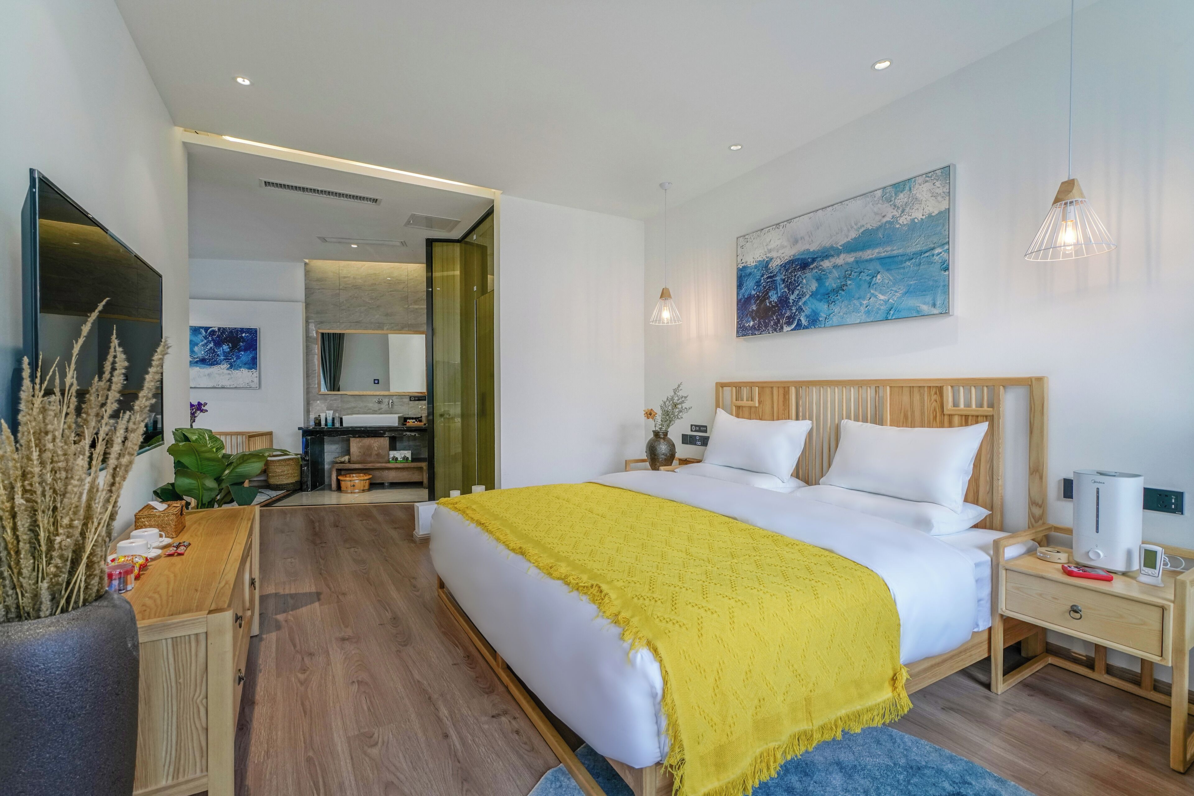 Une chambre d’hôtel moderne, dotée d’un grand lit, de tables de chevet, d’une télévision et d’une salle de bain visible à travers une porte ouverte.