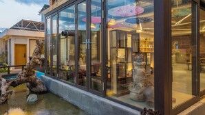 A modern building with large glass windows, a stone sculpture in the foreground, and a reflection of umbrellas inside. - Lijiang Xisu Garden (Lijiang)