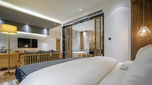 A modern hotel room with a large bed, a flat-screen TV, a wooden desk, and a bathroom visible through a sliding door. - Lijiang Xisu Garden (Lijiang)