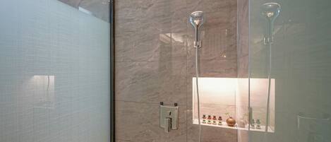 A modern bathroom with a glass shower enclosure, a handheld showerhead, a wall-mounted control panel, and a glass door.