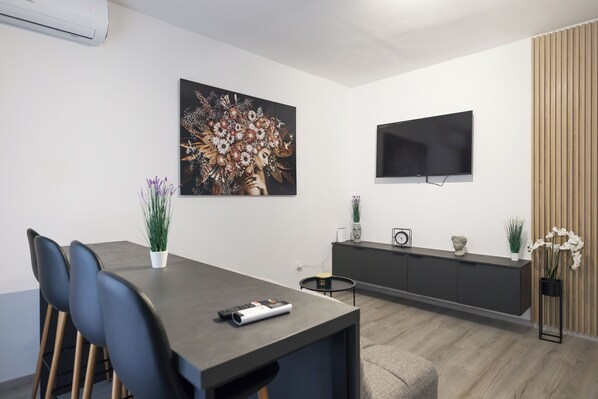 Ein modernes Wohnzimmer mit einem dunklen Holzesstisch, schwarzen Stühlen, einem Wand-Fernseher und einem großen Blumenbild.